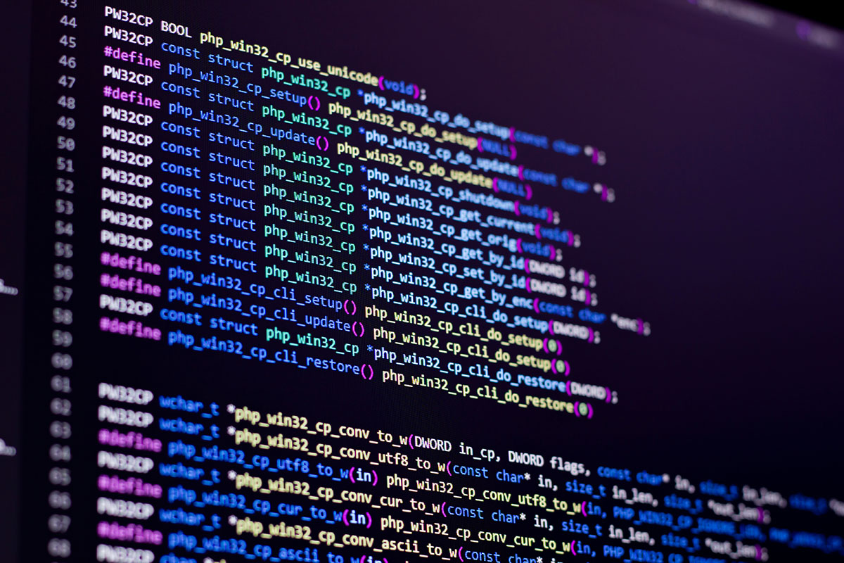 Close-up of a dark monitor showing lines of syntax-highlighted C source code from the PHP Windows codebase in blue, green and yellow