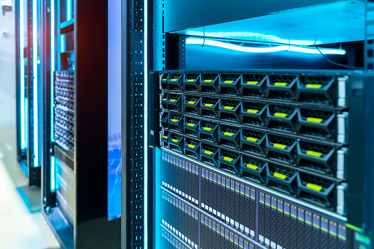 A dark server room aisle with rows of network racks lit by status indicator lights