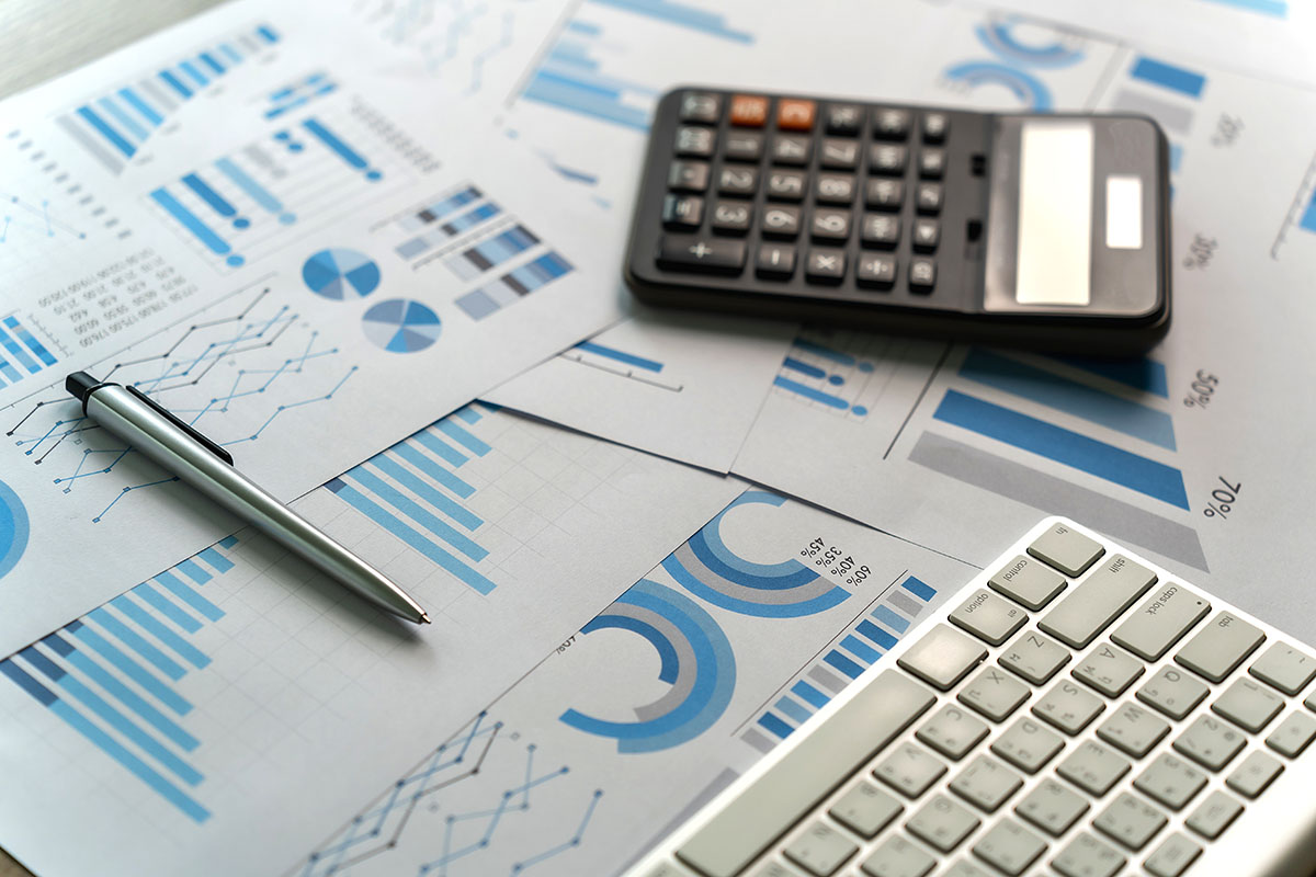 Printed financial charts, a calculator and a pen on a desk beside a keyboard