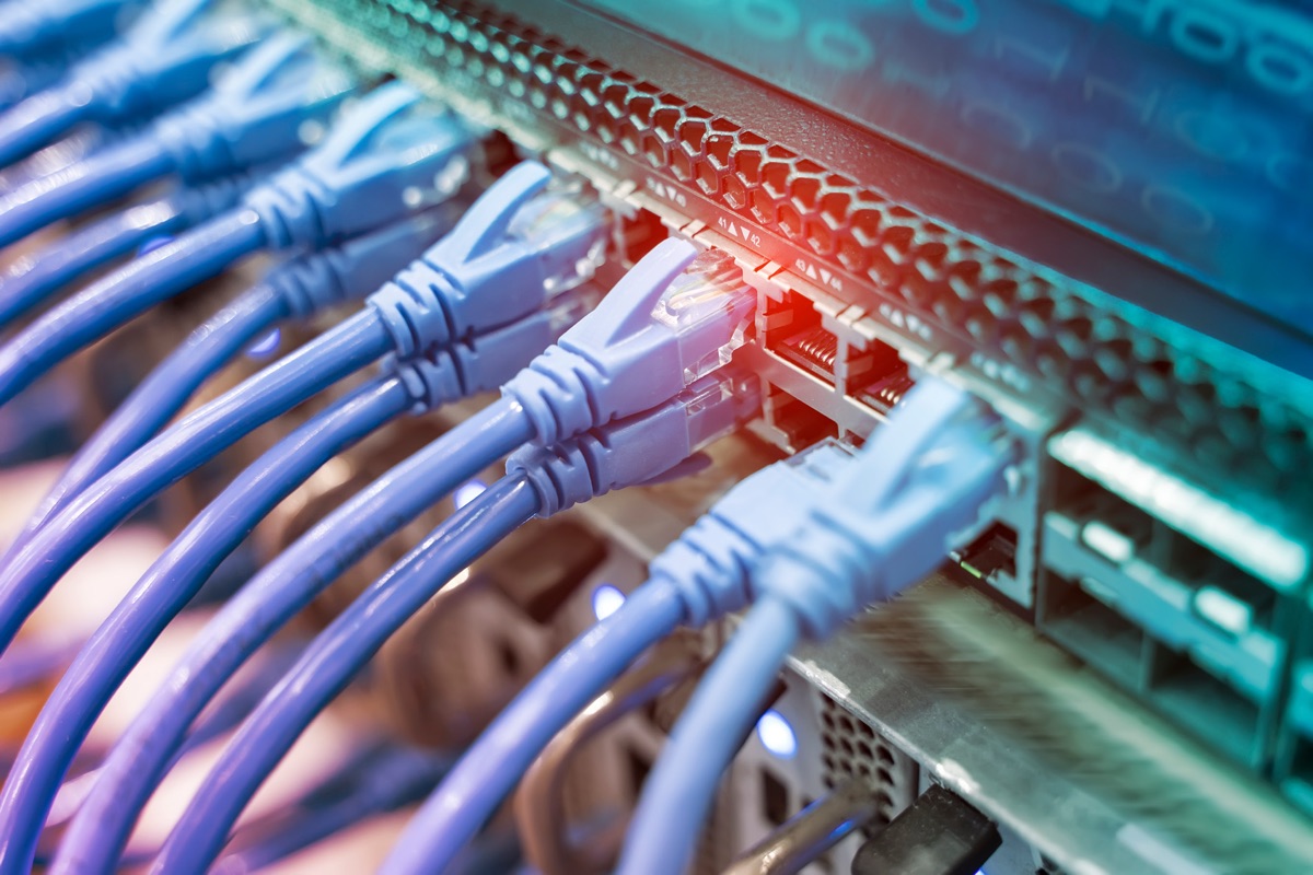 Close-up of blue ethernet patch cables plugged into a network core switch, with red and teal light glowing across the front panel
