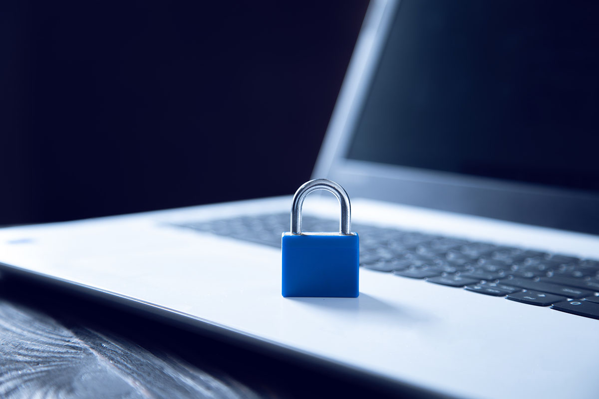 A small blue padlock standing on the palm rest of a silver laptop against a dark background