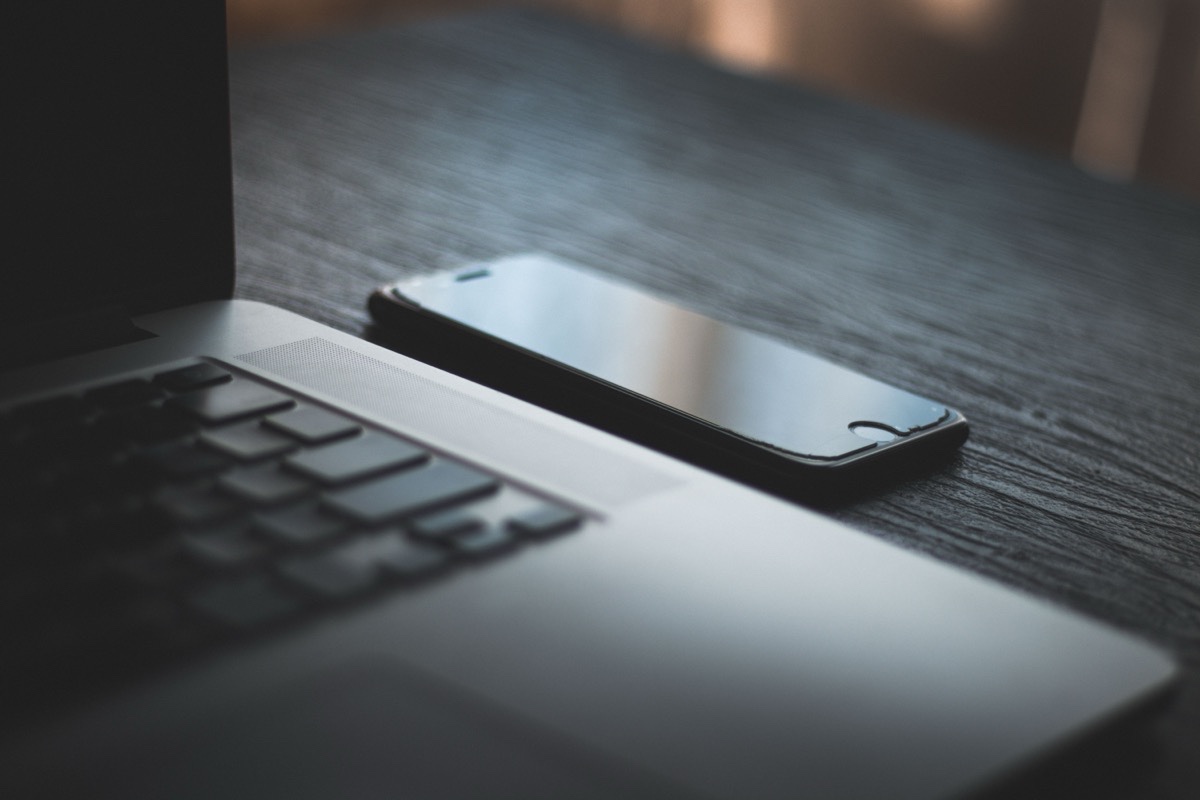 A smartphone lying beside a laptop keyboard on a dark desk in low light