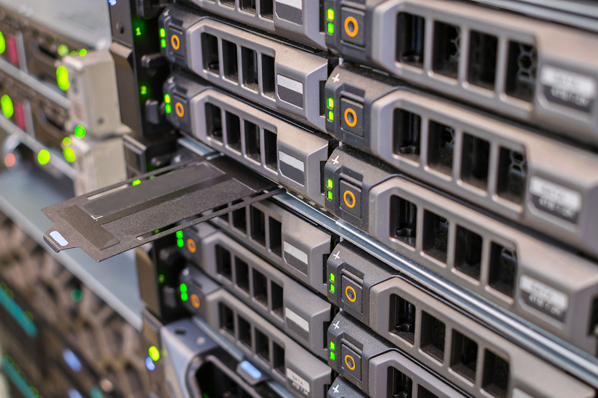 Close-up of rack-mounted servers with rows of hot-swap drive bays and green and orange status lights, one drive caddy pulled open