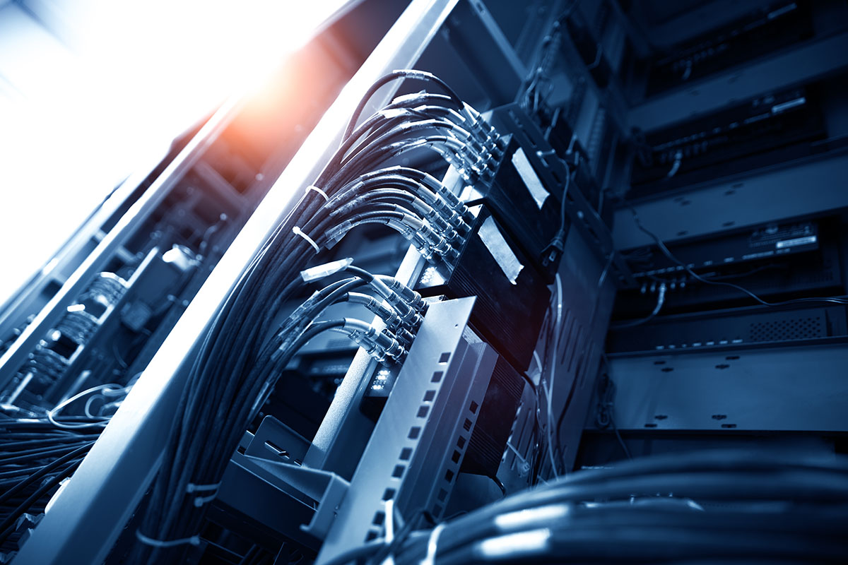 A tight angle on server rack cabling and patch panels in a data centre, lit blue with a lens flare