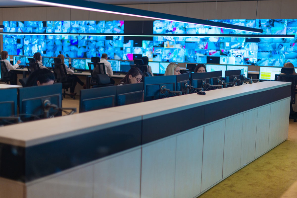 A large security operations centre with analysts at rows of monitors in front of a wall of blue video screens