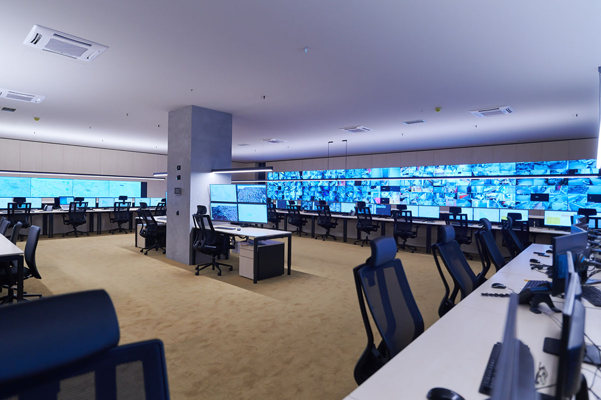 An empty security control room with a wall of monitors and rows of unoccupied desks