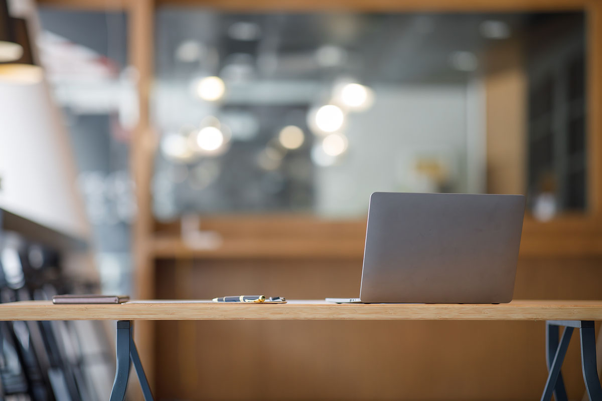 An open laptop left running on a desk in an empty open-plan office, its screen turned away